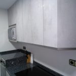 En este caso las puertas son en gris con un acabado un poco rugoso y encimera de granito de importación, dando luminosidad a la cocina con la vitrina en color blanco y dibujo al tono de la puerta
