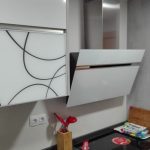 Una combinación de materiales, la zona de arriba blanco brillo y zona de abajo una puerta gris en mate y los decorativos también en gris,con tirador uñero en inox. y encimera de Silestone en color Marengo, vemos la vitrina en cristal blanco con decorado en el mismo color que la encimera.