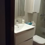 Esto es un baño, los muebles combinando blanco mate y madera en tono beige con tirador uñero